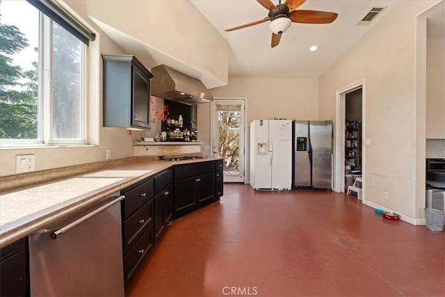 kitchen with concrete flooring, light countertops, appliances with stainless steel finishes, wall chimney range hood, and plenty of natural light