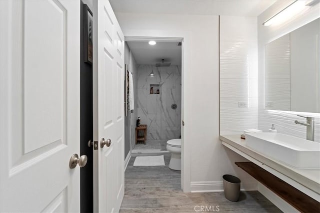 bathroom with a marble finish shower, baseboards, toilet, wood finished floors, and a sink