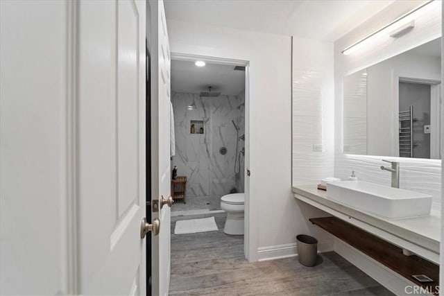 full bath featuring toilet, wood finished floors, a sink, baseboards, and a marble finish shower