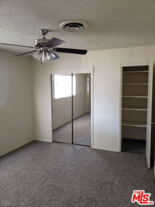 unfurnished bedroom with a walk in closet, carpet flooring, ceiling fan, a closet, and a textured ceiling