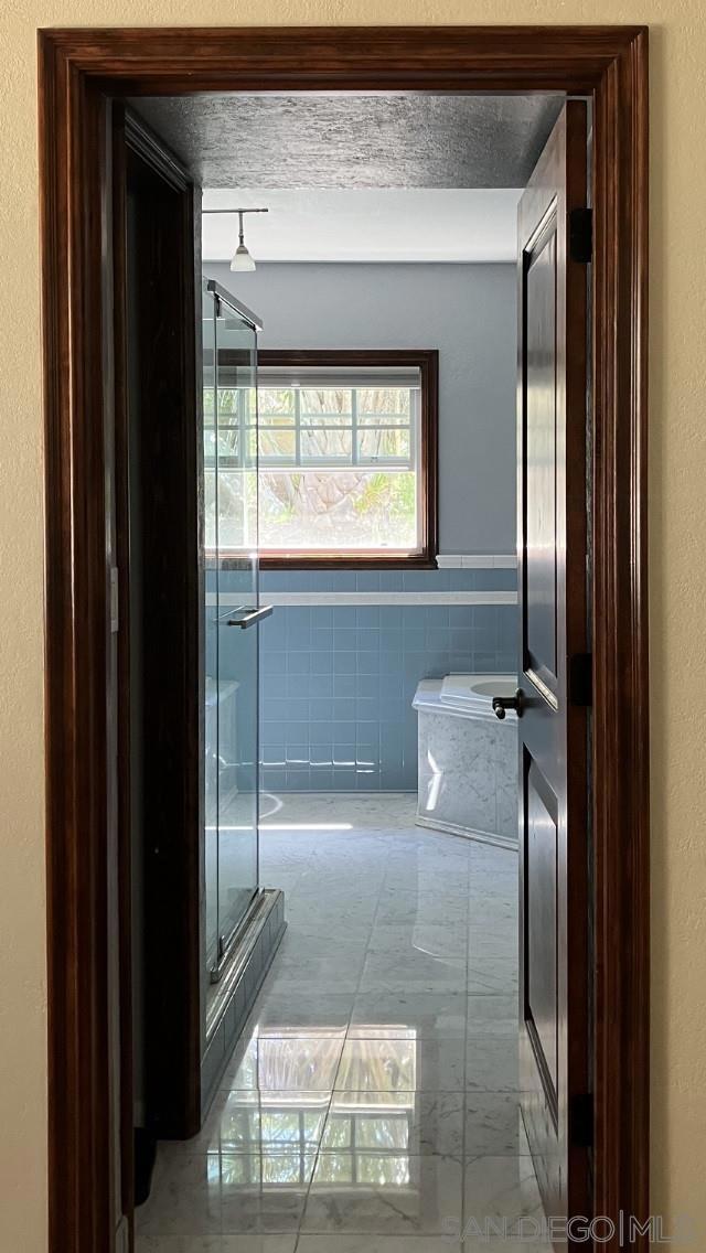 bathroom with a textured ceiling, plus walk in shower, and tile walls