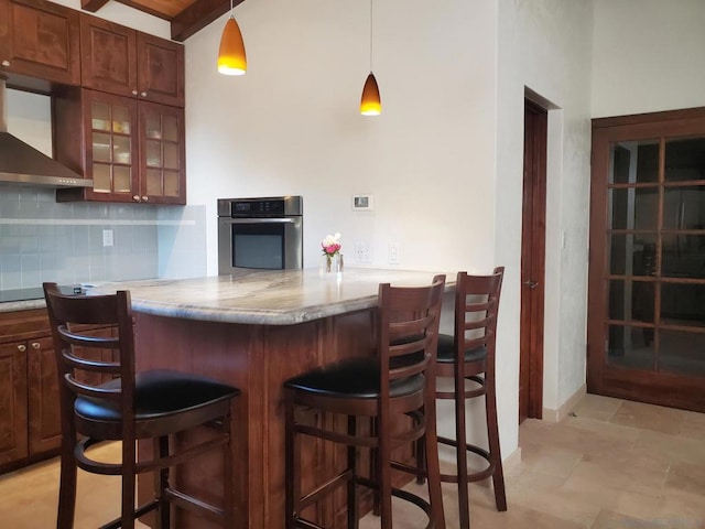 kitchen with pendant lighting, kitchen peninsula, wall chimney exhaust hood, oven, and a breakfast bar area