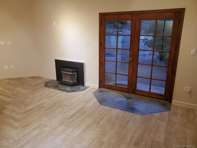 unfurnished living room with a wood stove, light hardwood / wood-style floors, and french doors