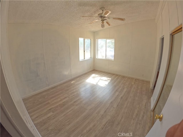 empty room with ceiling fan, light hardwood / wood-style floors, a textured ceiling, and vaulted ceiling