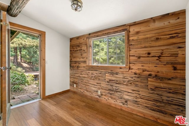 spare room featuring hardwood / wood-style floors, wood walls, and lofted ceiling