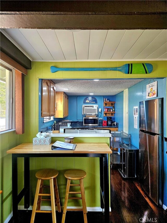 kitchen with appliances with stainless steel finishes, dark hardwood / wood-style flooring, a kitchen breakfast bar, kitchen peninsula, and butcher block countertops