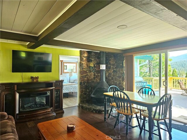 dining room with a fireplace, dark hardwood / wood-style floors, beamed ceiling, and a wood stove