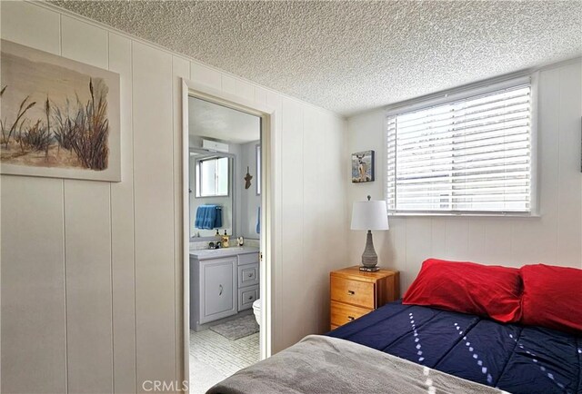 bedroom with a textured ceiling, ensuite bath, and wooden walls