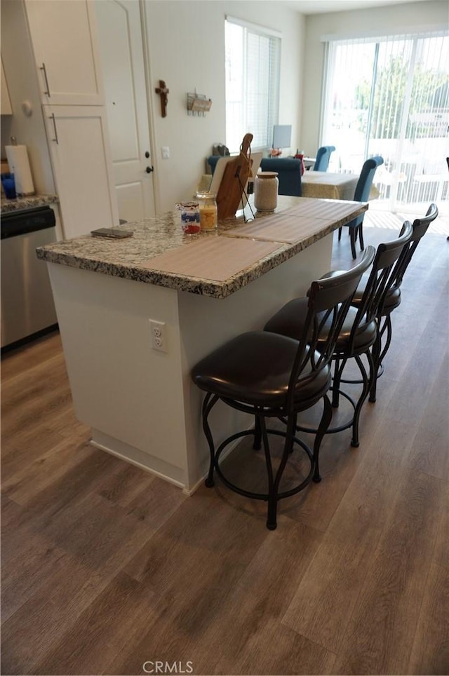 kitchen featuring a center island, white cabinets, stainless steel dishwasher, dark hardwood / wood-style floors, and a breakfast bar area