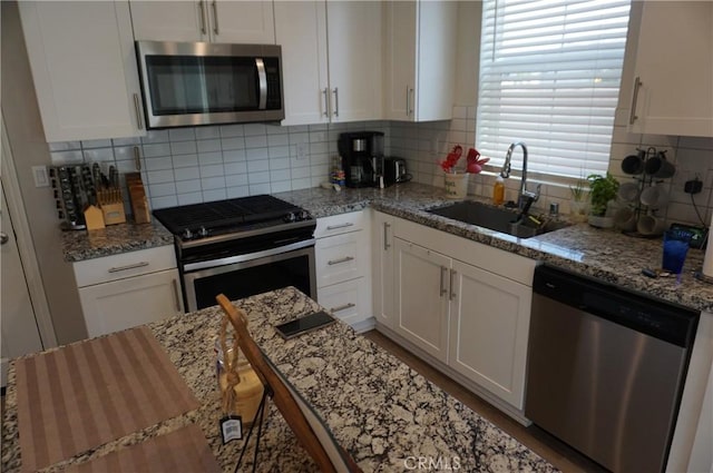 kitchen with sink, light stone counters, backsplash, white cabinets, and appliances with stainless steel finishes