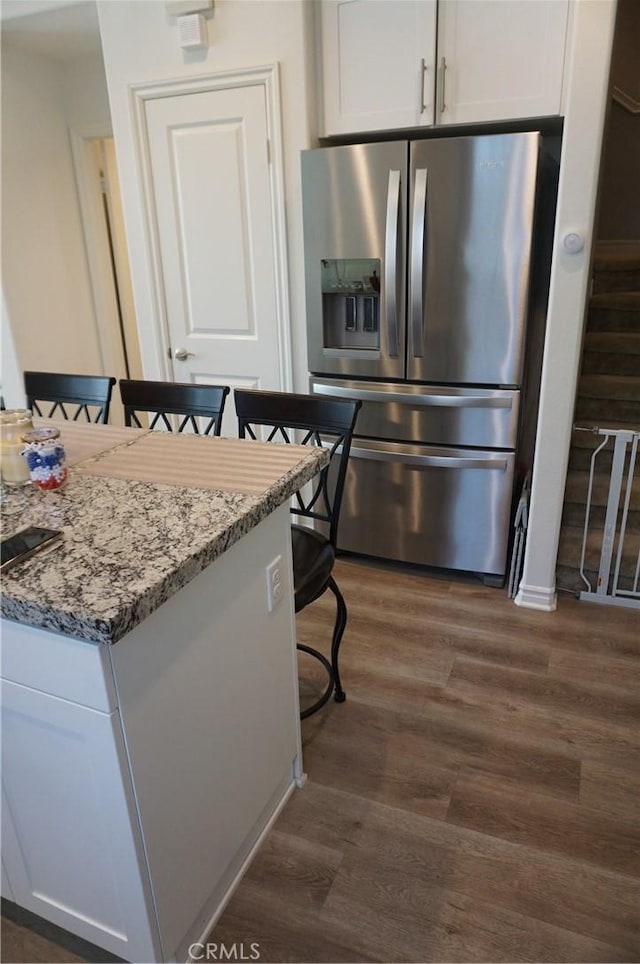 kitchen featuring stone countertops, a kitchen breakfast bar, white cabinetry, and stainless steel refrigerator with ice dispenser