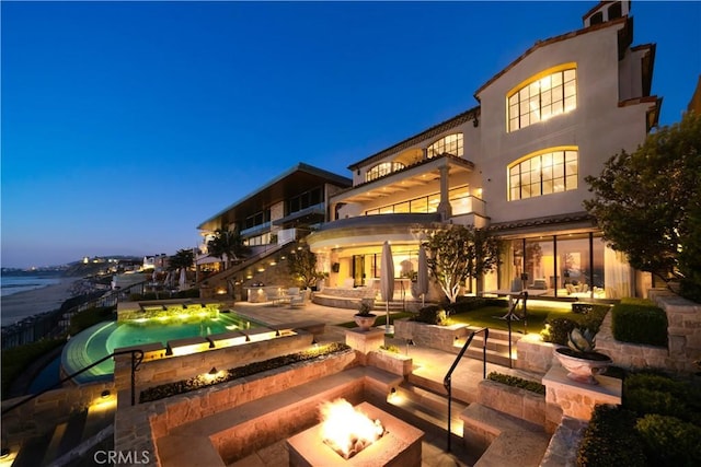 back house at dusk with a patio, a balcony, and an outdoor fire pit