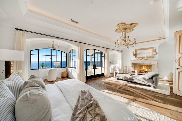 bedroom with a raised ceiling, wood-type flooring, a water view, an inviting chandelier, and a premium fireplace