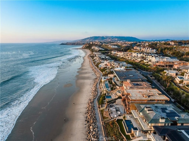 aerial view at dusk featuring a view of the beach and a water view