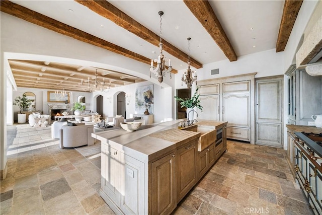 kitchen featuring a spacious island, sink, decorative light fixtures, beamed ceiling, and a chandelier