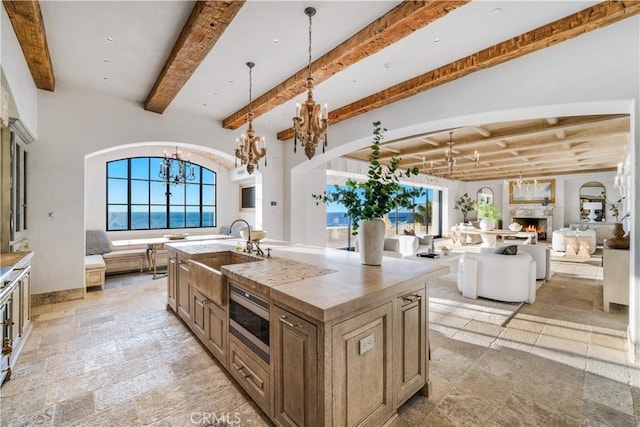 kitchen with a center island with sink, sink, beamed ceiling, decorative light fixtures, and a chandelier