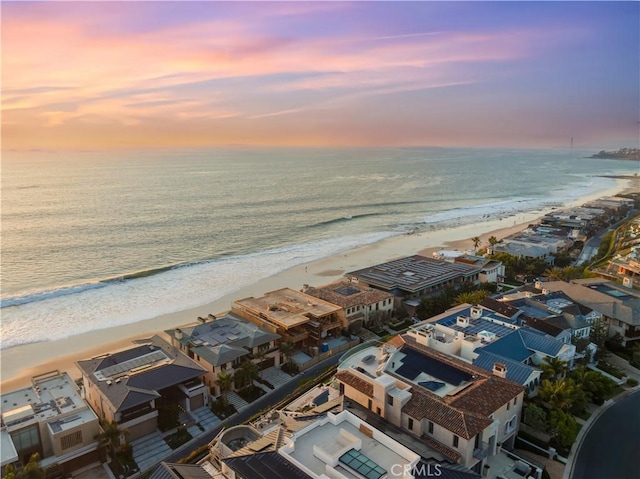 aerial view at dusk featuring a view of the beach and a water view