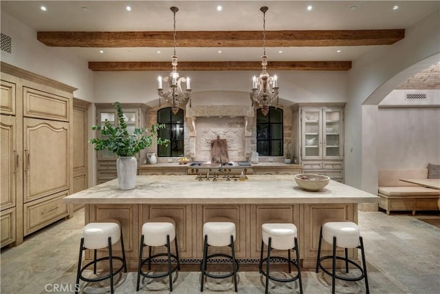 kitchen featuring a breakfast bar area, a large island with sink, light stone counters, and decorative light fixtures