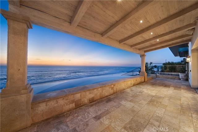 patio terrace at dusk featuring a water view and a view of the beach