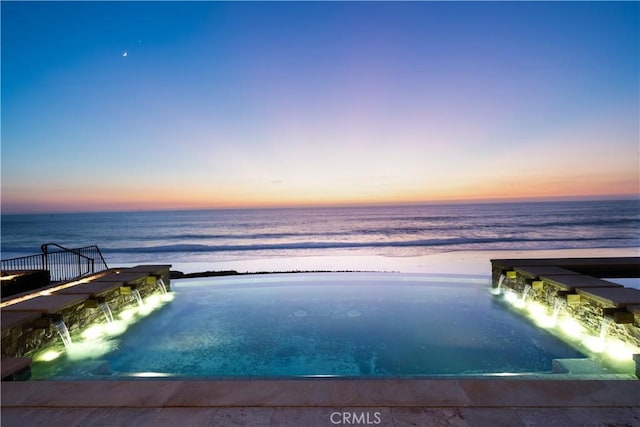 pool at dusk with pool water feature and a water view