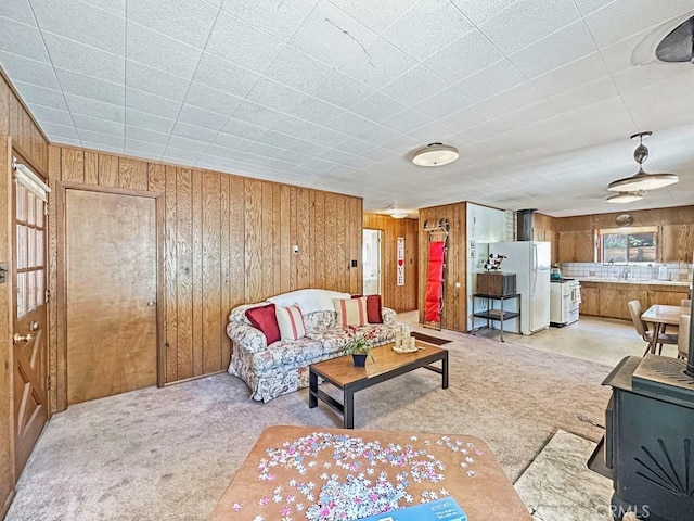 living room featuring light carpet, a wood stove, and wood walls