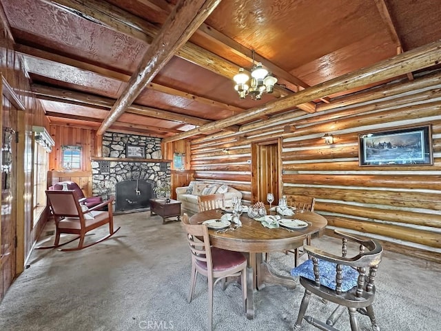 carpeted dining room with beam ceiling, rustic walls, wooden ceiling, a stone fireplace, and a notable chandelier