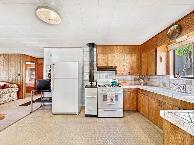 kitchen featuring tasteful backsplash, white appliances, wooden walls, sink, and tile countertops
