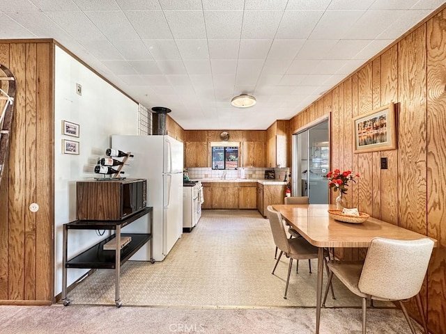 kitchen featuring white fridge, light carpet, wooden walls, and stainless steel range with gas stovetop