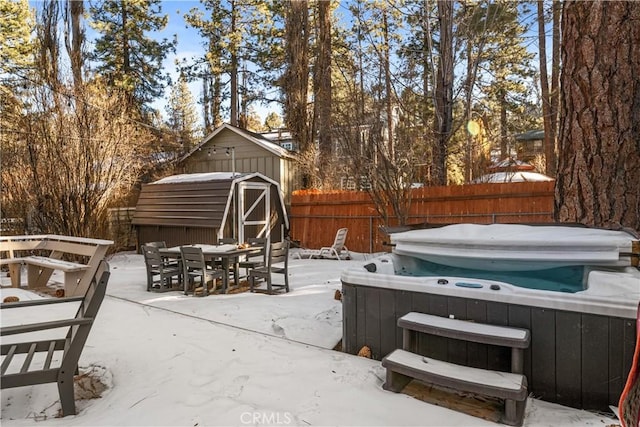 snow covered patio with a hot tub and a storage unit