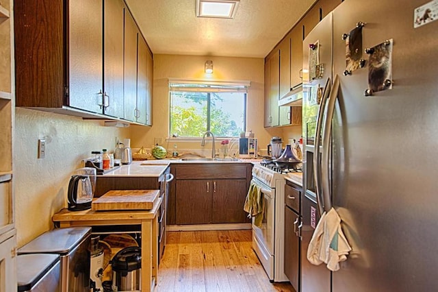 kitchen featuring light wood-type flooring, a textured ceiling, sink, stainless steel fridge with ice dispenser, and white gas stove