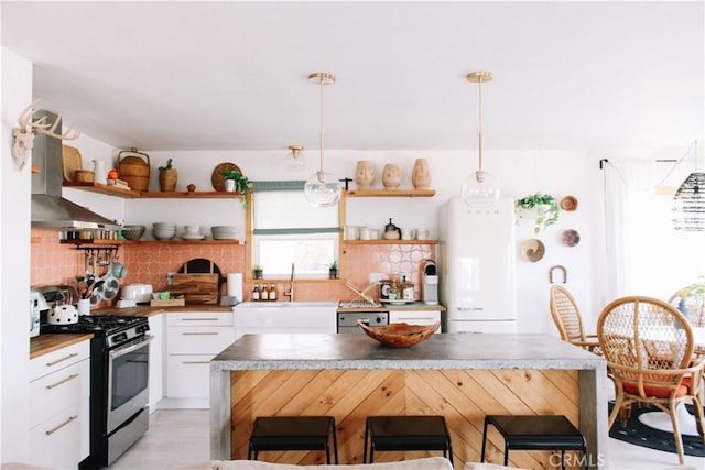 kitchen with sink, stainless steel range with gas cooktop, decorative light fixtures, a kitchen bar, and white cabinets