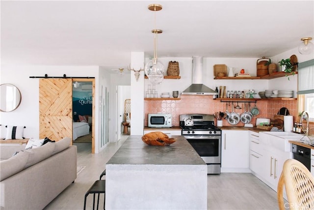 kitchen with white cabinets, ventilation hood, stainless steel range with gas cooktop, hanging light fixtures, and a barn door