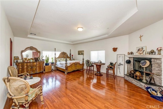 bedroom with a tray ceiling, multiple windows, and a stone fireplace