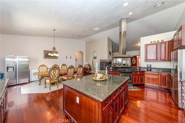 kitchen with wall chimney exhaust hood, vaulted ceiling, appliances with stainless steel finishes, and dark wood-type flooring