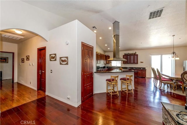 kitchen with arched walkways, dark countertops, visible vents, island range hood, and a peninsula