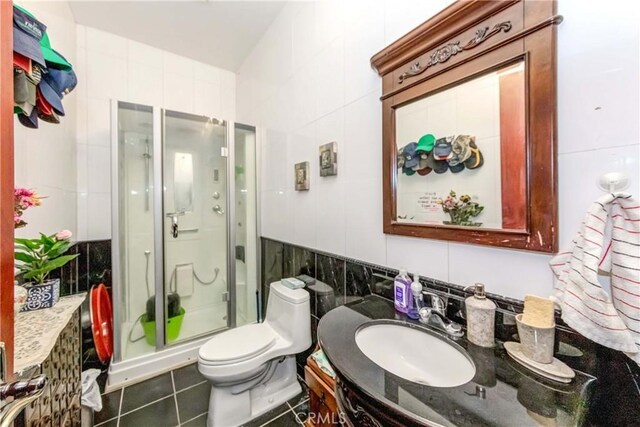 bathroom with vanity, tile walls, tile floors, a shower with door, and toilet