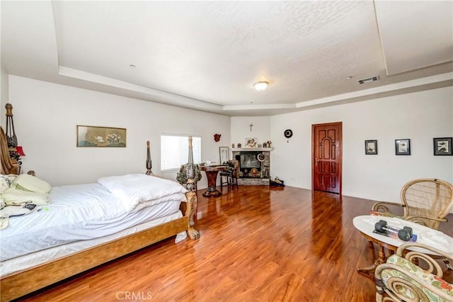 bedroom featuring a glass covered fireplace, a raised ceiling, visible vents, and wood finished floors