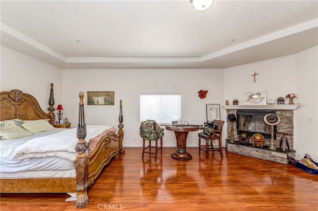 bedroom with a raised ceiling, dark hardwood / wood-style floors, and a stone fireplace