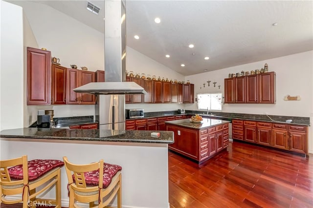 kitchen with kitchen peninsula, dark hardwood / wood-style floors, appliances with stainless steel finishes, a kitchen island, and island exhaust hood