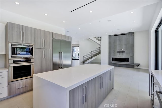 kitchen with light tile floors, a center island, a large fireplace, and built in appliances