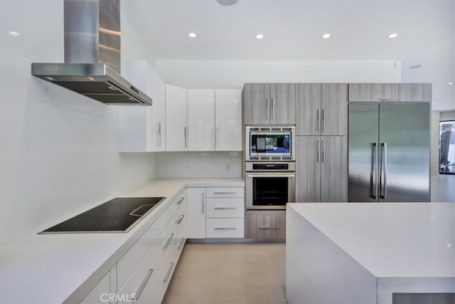 kitchen with light tile floors, white cabinetry, wall chimney exhaust hood, and built in appliances