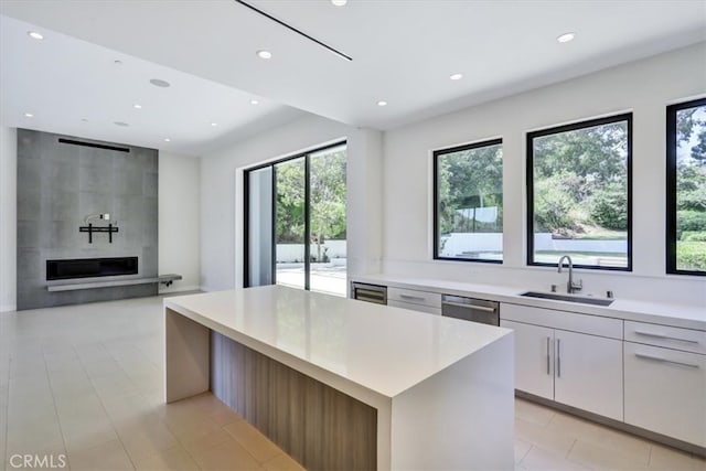 kitchen with sink, light tile floors, a kitchen island, white cabinets, and a large fireplace