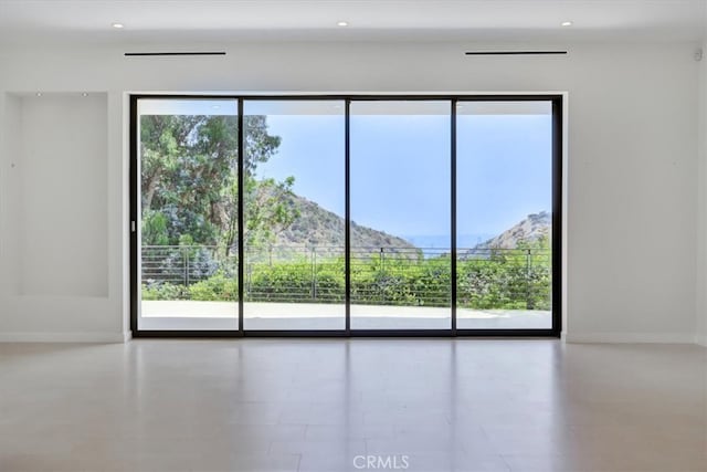 empty room with a healthy amount of sunlight, a mountain view, and light tile floors