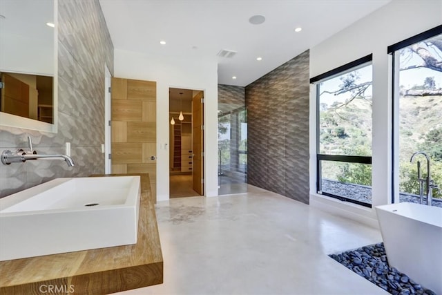 bathroom with concrete floors, tasteful backsplash, a bath, tile walls, and sink