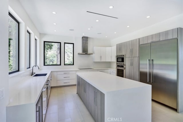 kitchen featuring built in appliances, sink, light tile floors, a kitchen island, and wall chimney exhaust hood