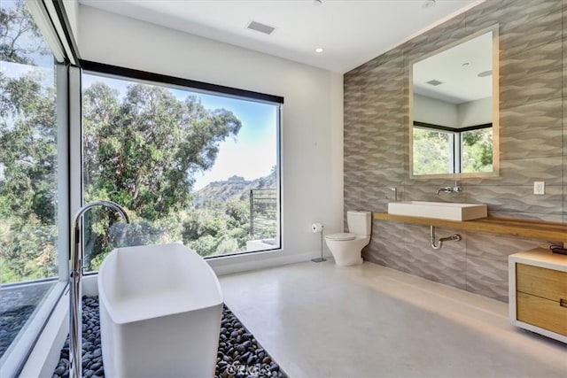 bathroom with plenty of natural light, toilet, concrete floors, and large vanity