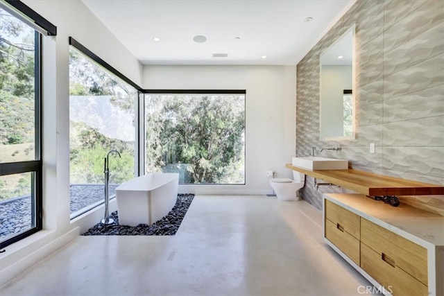 bathroom featuring tile walls, toilet, a healthy amount of sunlight, and concrete flooring