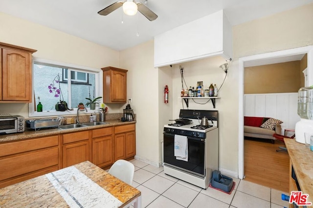 kitchen with ceiling fan, white gas stove, light hardwood / wood-style floors, and sink