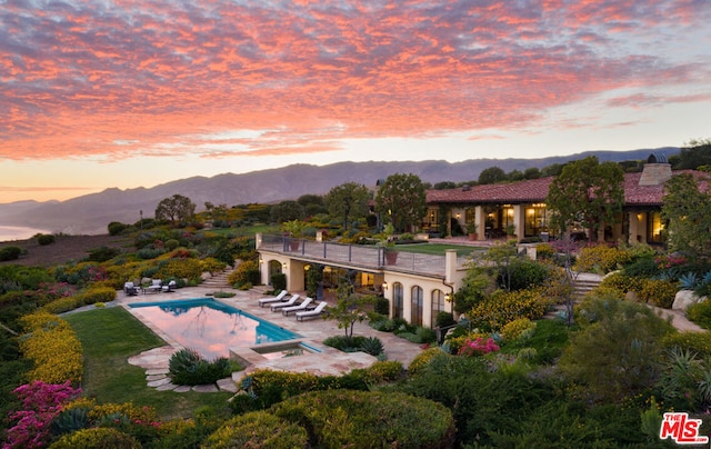 pool at dusk featuring a mountain view, a patio area, and an in ground hot tub