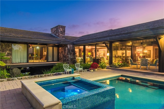 pool at dusk with a patio and an in ground hot tub